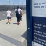Immigrants arriving at an in intake shelter walk by signs stating that their conversations are being recorded.