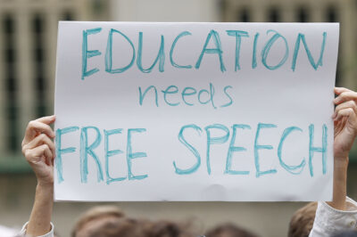 A student holds up a placard reading 'Education needs free speech' while attending a march.