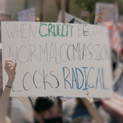 A demonstration sign that say "When Cruelty Becomes Normal, Compassion Looks Radical."