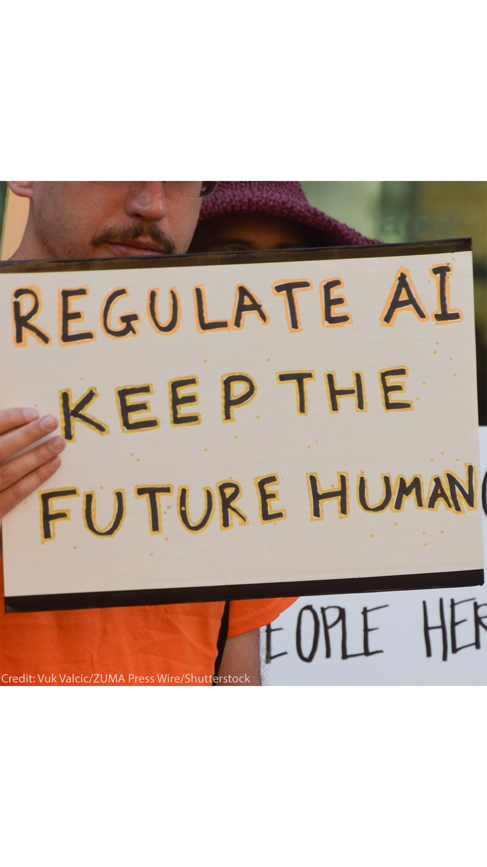 The camera focuses on a sign held by a demonstrator that reads, "REGULATE AI KEEP THE FUTURE HUMAN."