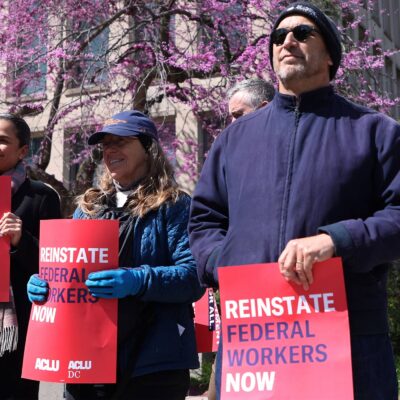 Demonstrators hold signs from ACLU & ACLU DC that read" REINSTATE FEDERAL WORKERS NOW" and "EQUAL AND JUST TREATMENT FOR ALL" as they protest in support of Federal Workers at the Office of Personnel Management in Washington, DC.