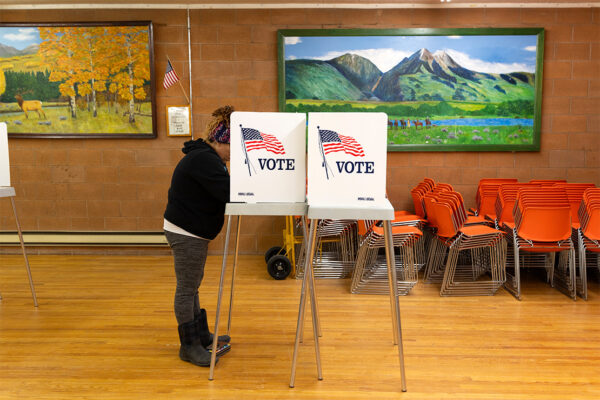 A woman with her face hidden stands in front of a voting table.